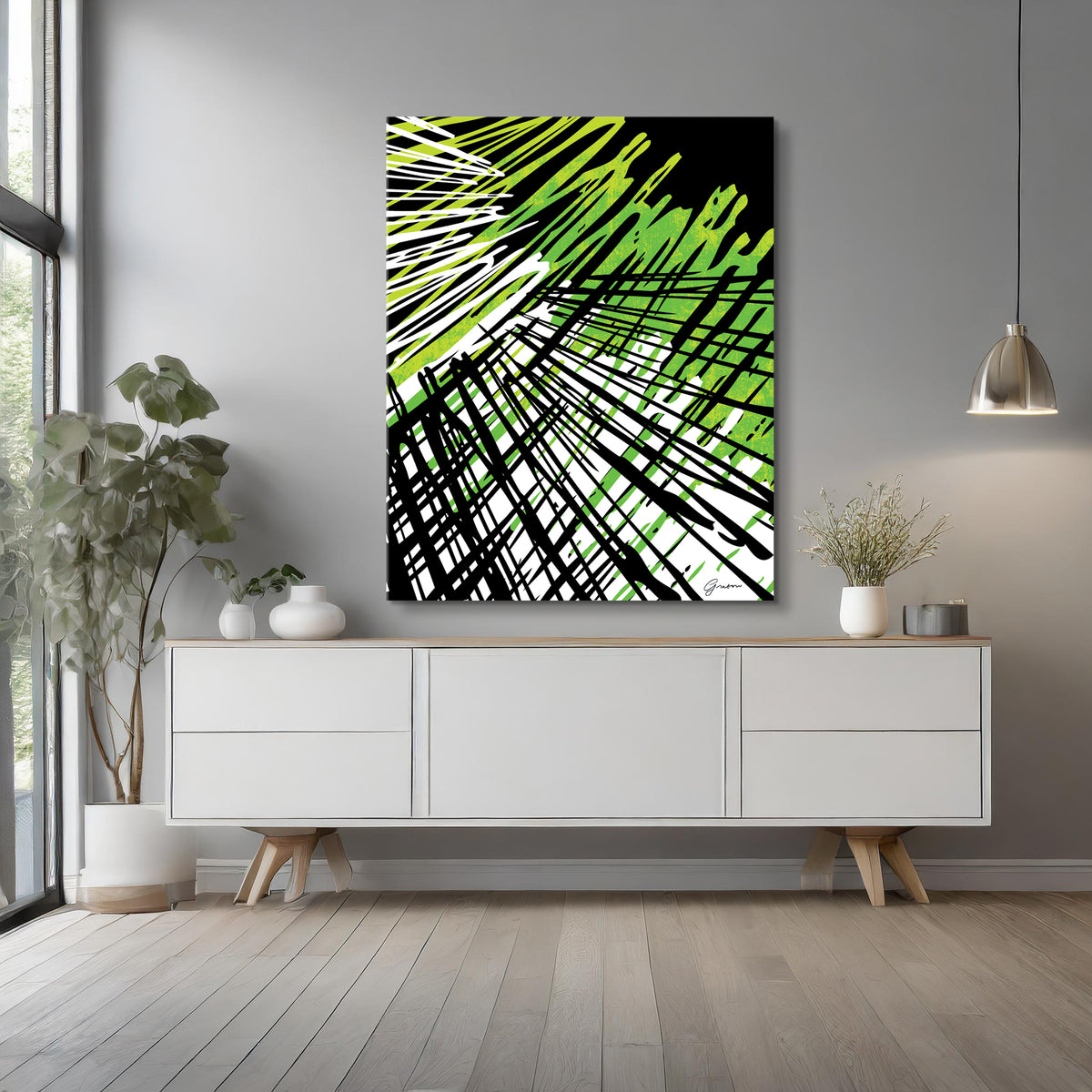 The image showcases a modern interior with a minimalist aesthetic. A bold abstract canvas hangs on a light gray wall, featuring a dynamic mix of black, white, and green intersecting lines and brushstrokes, creating an energetic and contemporary feel. Below the artwork, a sleek white sideboard with wooden legs adds to the clean, modern look. The space is accented with subtle decor, including white vases, a potted plant, and a pendant light, enhancing the room's elegant simplicity.