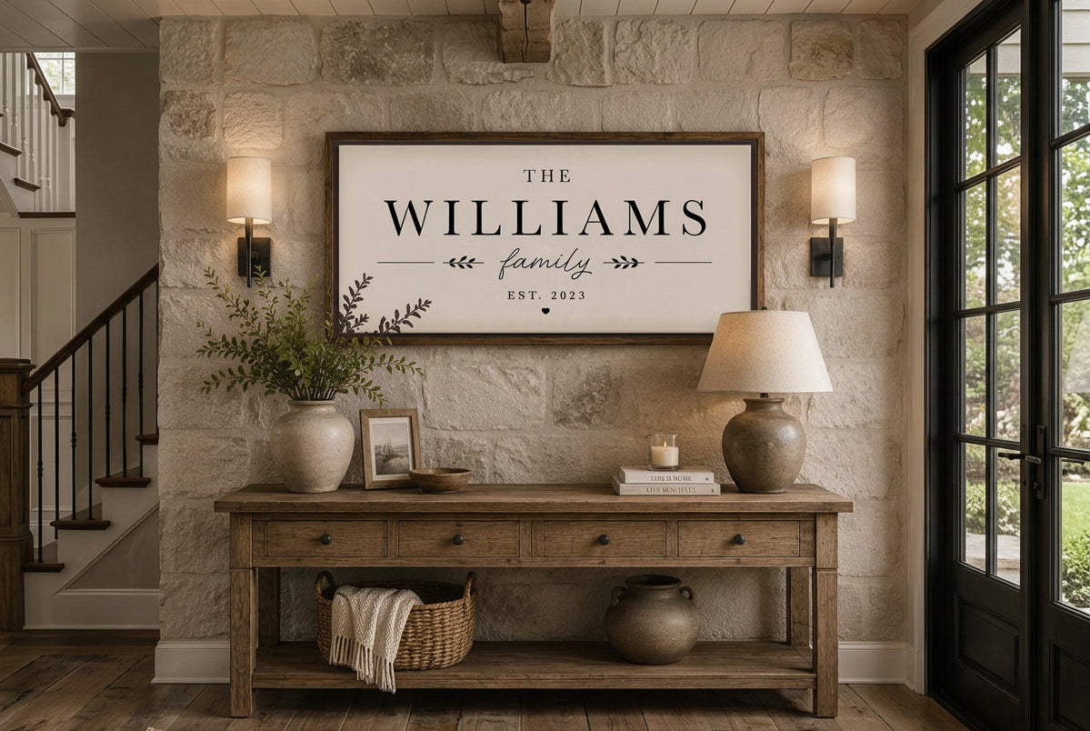 A framed personalized sign reading 'THE WILLIAMS family EST. 2023' hangs on a stone wall above a rustic wooden console table in a styled home entryway.