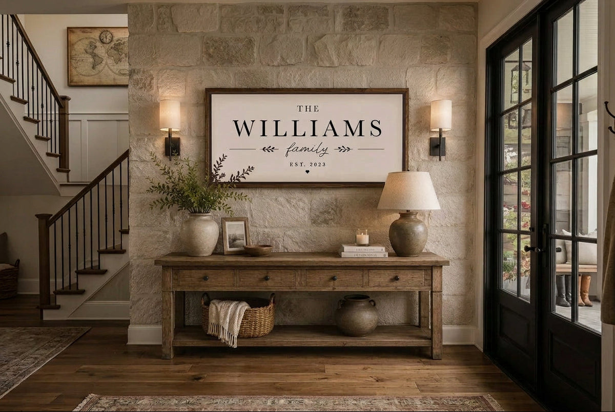 A framed personalized wall sign reading 'THE WILLIAMS family EST. 2025' hangs above a rustic wooden console table in a stone-walled entryway.